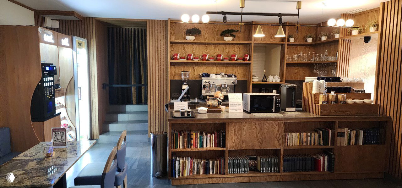 Интерьер зоны самообслуживания в небольшом московском отеле: стойка с кофемашиной, вендинговый автомат, полки и столы.