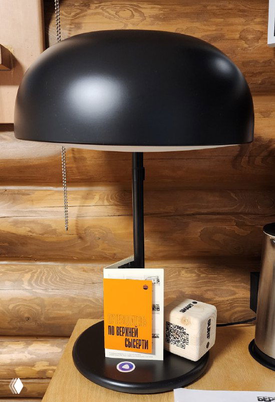 Прикроватная лампа в гостиничном номере; под ней подставка с стильной книгой в оранжевой обложке и небольшим декоративным кубом, интерьер.