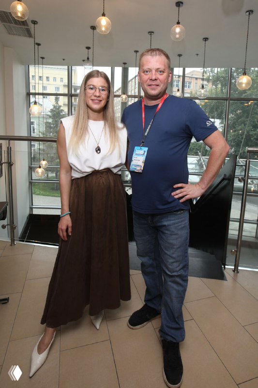 Организатор и участница конференции в фойе на фоне больших окон: деловой кадр после сессий, Москва, фитнес-сообщество, деловая атмосфера.