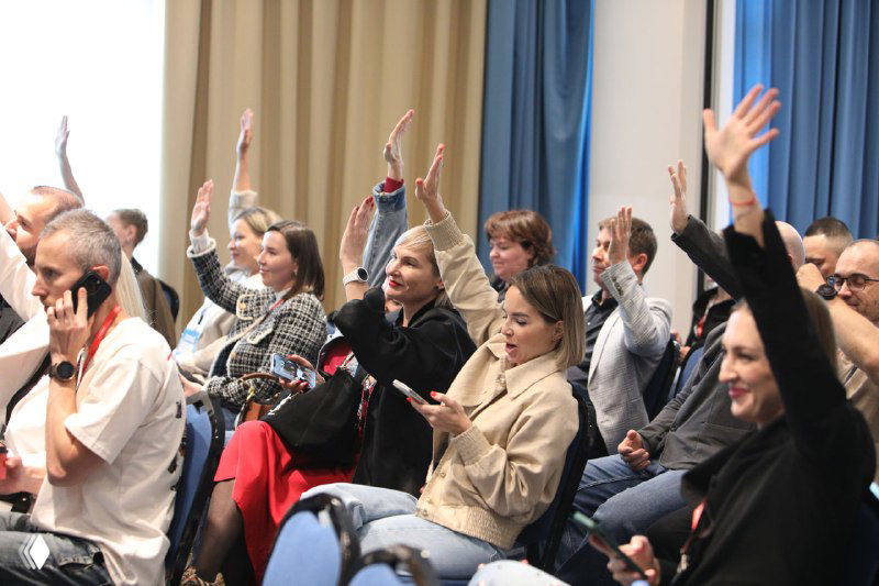 Зал с участниками конференции: люди поднимают руки, вовлечённый обмен мнениями и вопросы в рамках сессии, живое обсуждение кейсов.