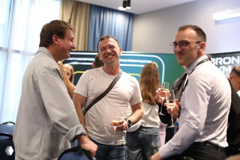 Группа людей в неформальной части конференции: улыбки, общение у фуд-корта или брейк-аута, нетворкинг и обмен контактами.