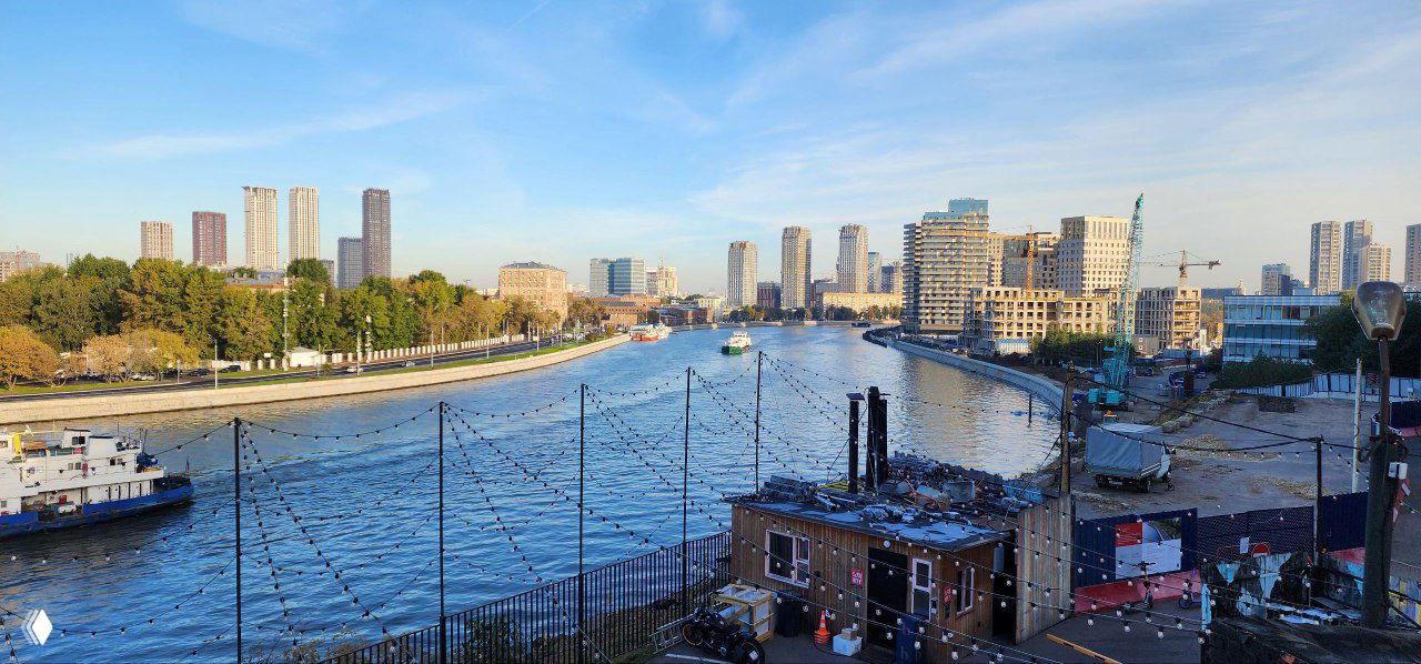 Панорамный вид на набережную и городской пейзаж рядом с локацией ивента: река, высотные здания, причал и подготовительная зона мероприятия.