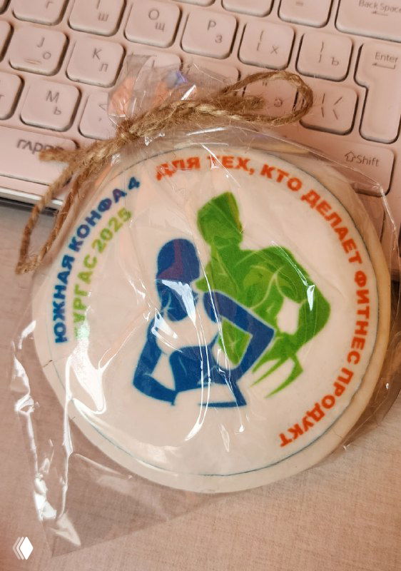 Пряник с печатью: силуэты мужчины и женщины и брендовый текст по кругу, упакован в целлофан, лежит на клавиатуре.