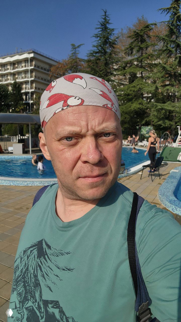 Селфи организатора у бассейна DFC Sochi: лицо в бандане на фоне водной зоны и гостиничной инфраструктуры, солнечный день.