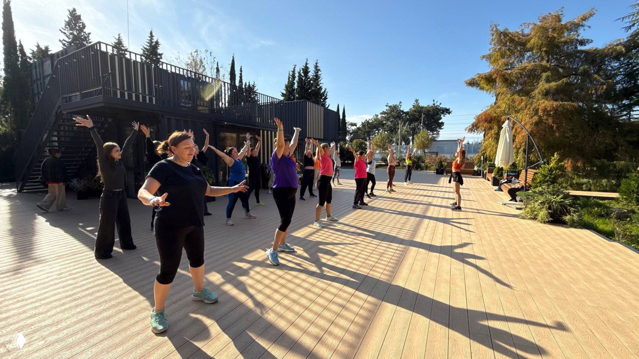 Утренняя уличная площадка DFC Sochi: группа участников выполняет танцевальные упражнения на открытой террасе под солнцем.