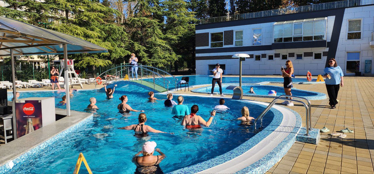 Аквазумба в бассейне DFC Sochi: участницы в воде выполняют упражнения, тренер на бортике даёт команды, видно бассейную инфраструктуру.