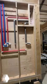 Фрагмент каркасной стены модульного дома с трубами и деталями системы отопления, видны крепления и монтажные короба внутри стены при сборке.