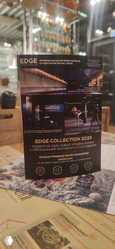 Рекламный тейблтент клуба EDGE на столе ресторана в интерьере: премиальный макет с логотипом и визуалом клуба как пример оффлайн‑онлайн маркетинга.
