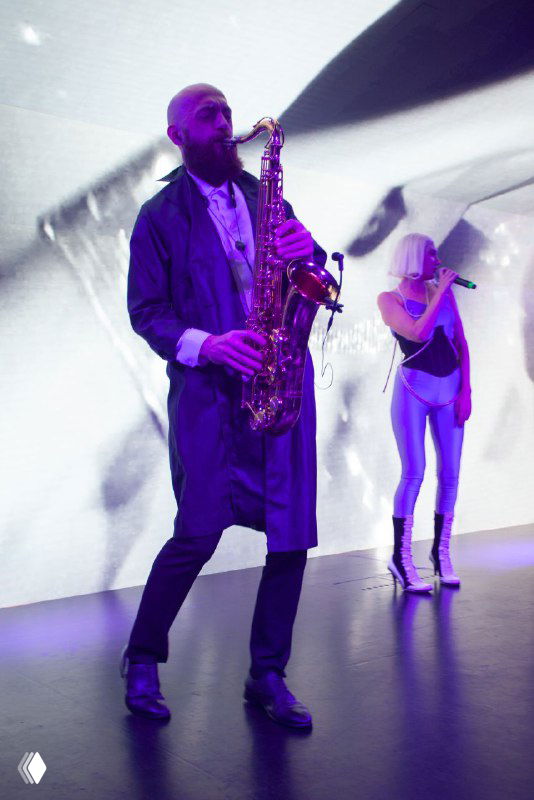 Саксофонист в костюме и вокалистка на сцене в шоу-программе Bright Conf, крупный план музыкального номера в вечерней части конференции.