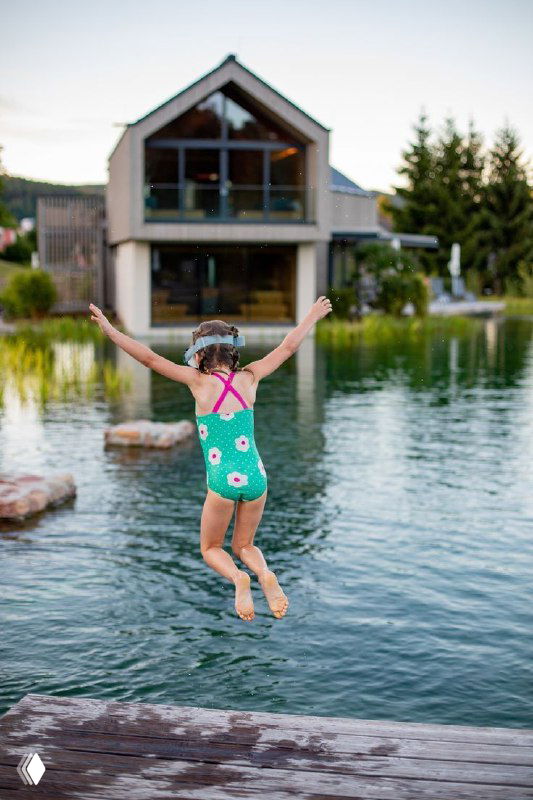 Ребёнок в купальном костюме прыгает с причала в озеро рядом с гостиницей — живой кадр, передающий удовольствие и семейный отдых.