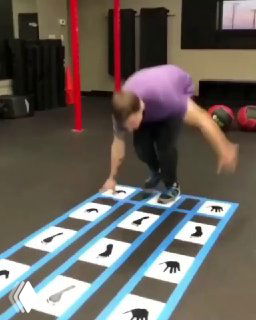 Человек в зале проходит маршрут из листов А4 и скотча с силуэтами рук и стоп; в кадре — прыжок участника.