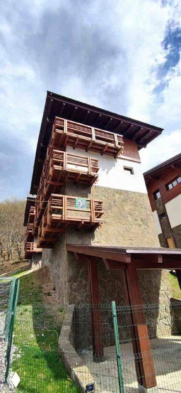 Фасад многоэтажного гостевого дома в Сочи с деревянными балконами и каменной облицовкой на фоне пасмурного неба.