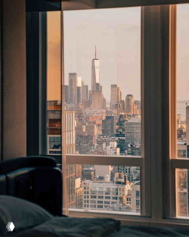 Утренний городской вид через окно номера на силуэты высоток — спокойный кадр, создающий ожидание завтрака с видом.
