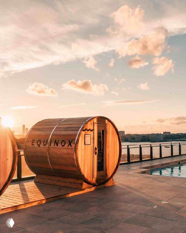 Уличная терраса отеля с зонами отдыха и бочкообразными спа-капсулами Equinox на фоне заката — элемент wellness-концепции.
