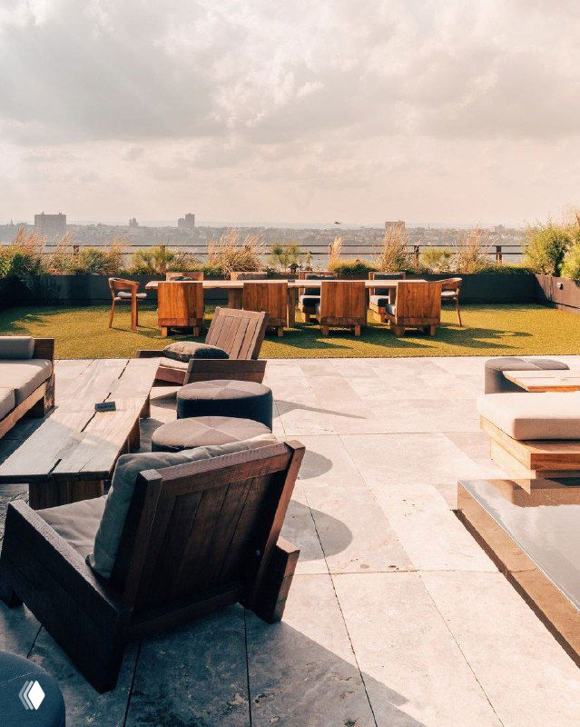 Дневная панорамная терраса с деревянной мебелью и зоной отдыха, создающая представление о релаксе на крыше городского отеля.