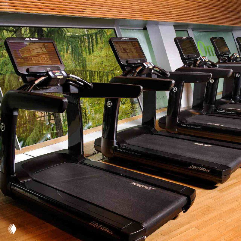 Ряд элитных беговых дорожек в просторном зале велнес‑клуба First & Only в Москве, современный дизайн и тёплые деревянные элементы пола.