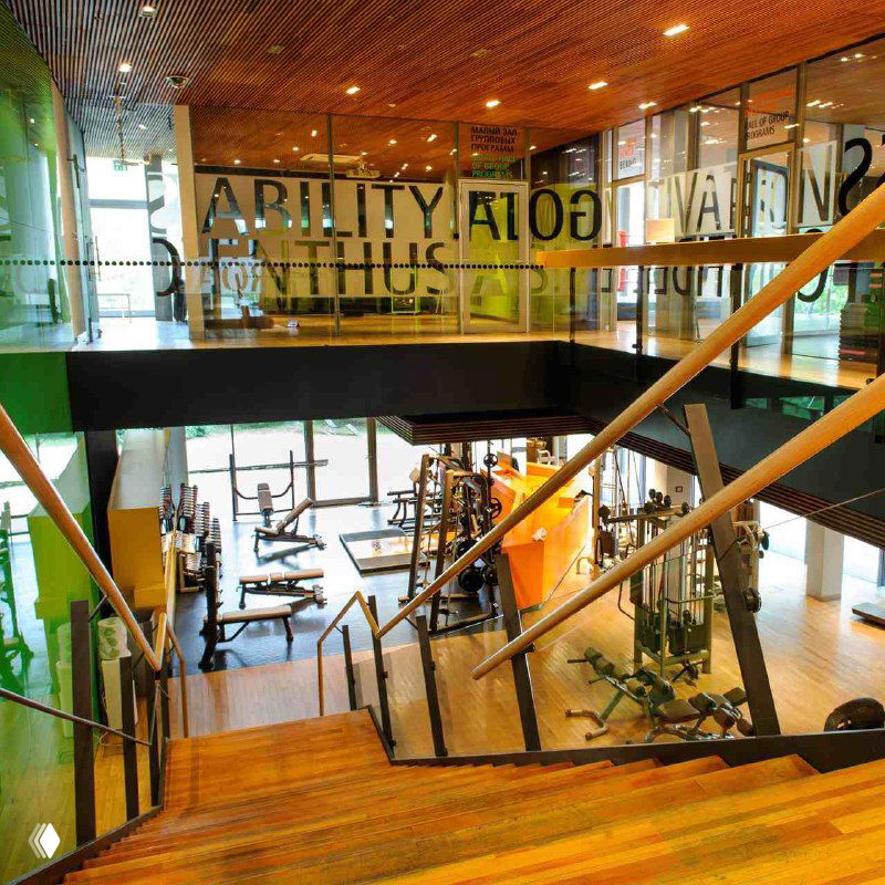 Вид с лестницы на тренажёрный зал First & Only: свободное пространство с кардиозоной, тренажёрами и зелёными акцентами в интерьере.