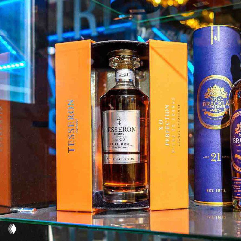 Крупный план эксклюзивной бутылки крепкого напитка на витрине Wine Store внутри велнес‑клуба First & Only, упаковка как подарок.