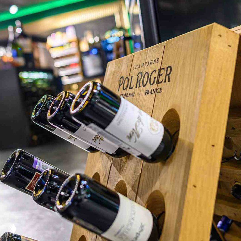 Деревянная стойка с винными бутылками и видимыми этикетками в Wine Store при First & Only — ассортимент вин и деликатесов для покупки и дегустации.