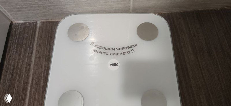 Электронные весы на полу номера с короткой надписью над ними, минималистичный предмет интерьера и фирменная подача текста отеля Ays.