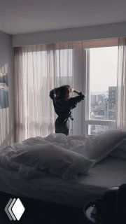 Человек у окна в номере отеля, растрёпанная постель на переднем плане и городской вид за шторами — кадр из видео Equinox.