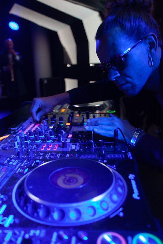 Диджей за пультом в синем свете клубной подсветки — развлекательная часть ивента, музыкальное сопровождение вечеринок.