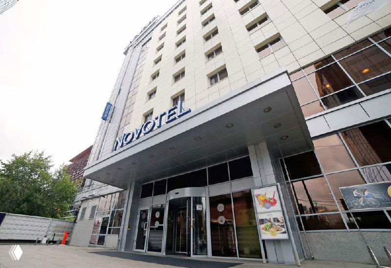 Вход в отель с вывеской Novotel и стеклянной дверью — наглядный пример варианта размещения для участников события в Екатеринбурге