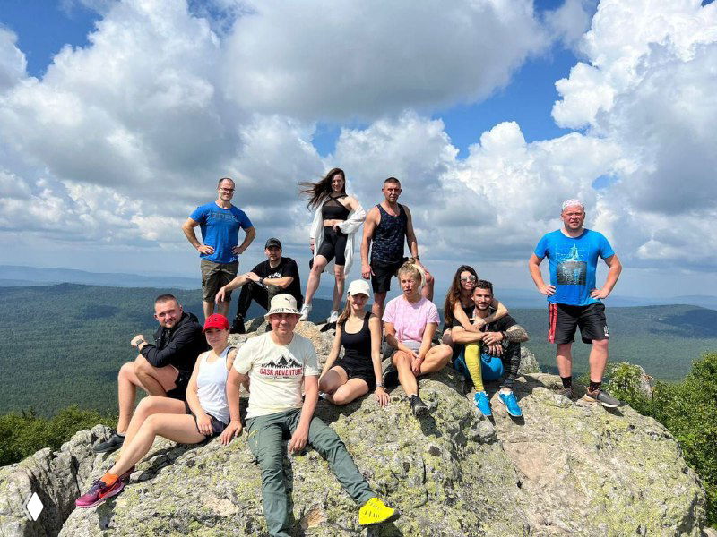 Группа туристов на вершине скалы: люди позируют на каменистом гребне под большим небом — пример пользовательской съёмки для отеля.