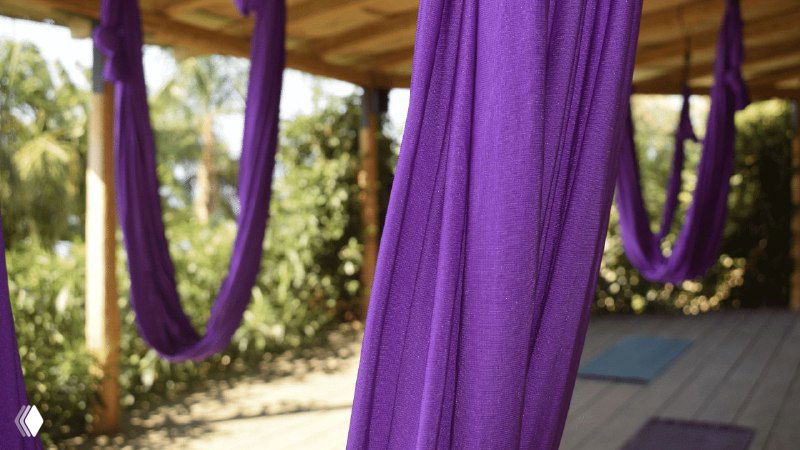 Фиолетовые тканевые гамак-петли для аэройоги, висящие на вертикальной конструкции в зоне с деревянным полом — пример гибкой фитнес-инфраструктуры.