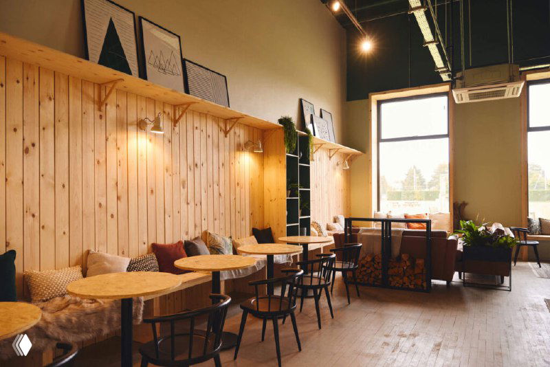 Зона отдыха и кафе в клубе: деревянная обшивка, столы и мягкие кресла, пространство для общения и релаксации вне тренировок, тёплая атмосфера.