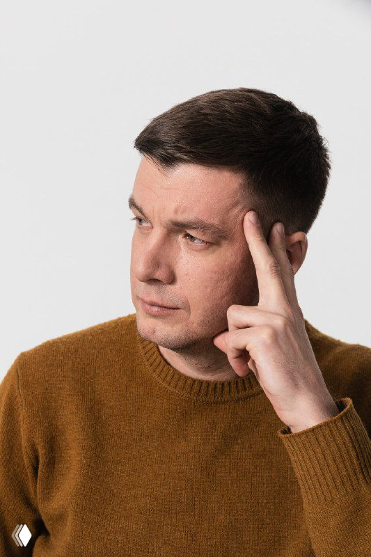 Портрет задумчивого мужчины в коричневом свитере, держащего руку у виска на нейтральном фоне; иллюстрация к теме различия эмоционального и физического голода.