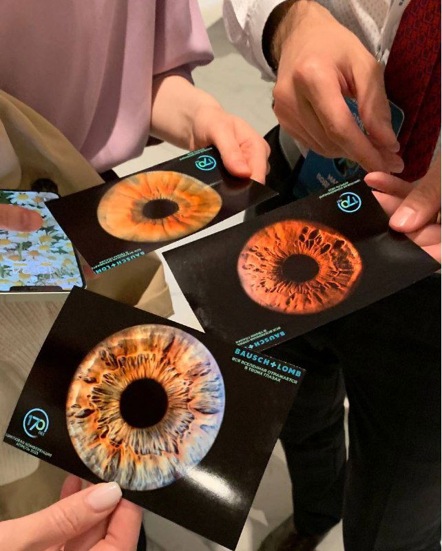 Несколько отпечатанных макрофотографий радужки глаза в руках участников на мероприятии — пример брендированных фотосувениров.