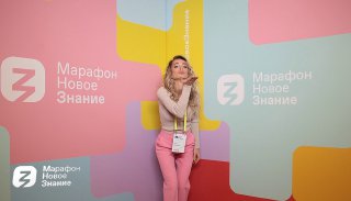 Девушка в розовом костюме позирует у цветной бренд‑стены «Марафон Новое Знание», пример оформления стенда и фотофона для ивента и промоакции.