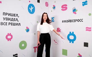 Участница позирует перед брендированным пресс‑воллом в концертном зале Зарядье; на фоне видны декоративные графические элементы, логотипы и хештеги мероприятия.