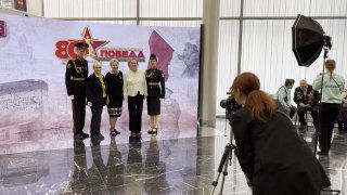 Фотосъёмка у крупного светодиодного экрана с оформлением «Победа»: несколько людей в форме и посетители на фоне LED‑панели внутри зала.