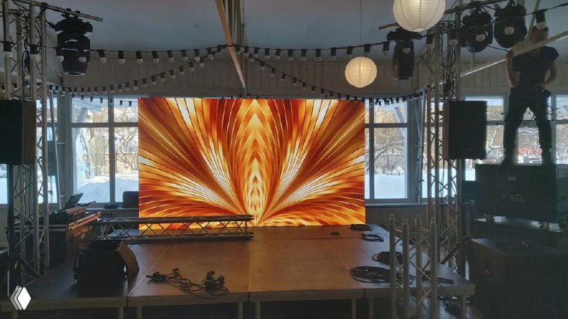 Сцена с крупным светодиодным экраном в зале: на экране абстрактная золотистая графика, вокруг монтажное оборудование и стойки для сцены.