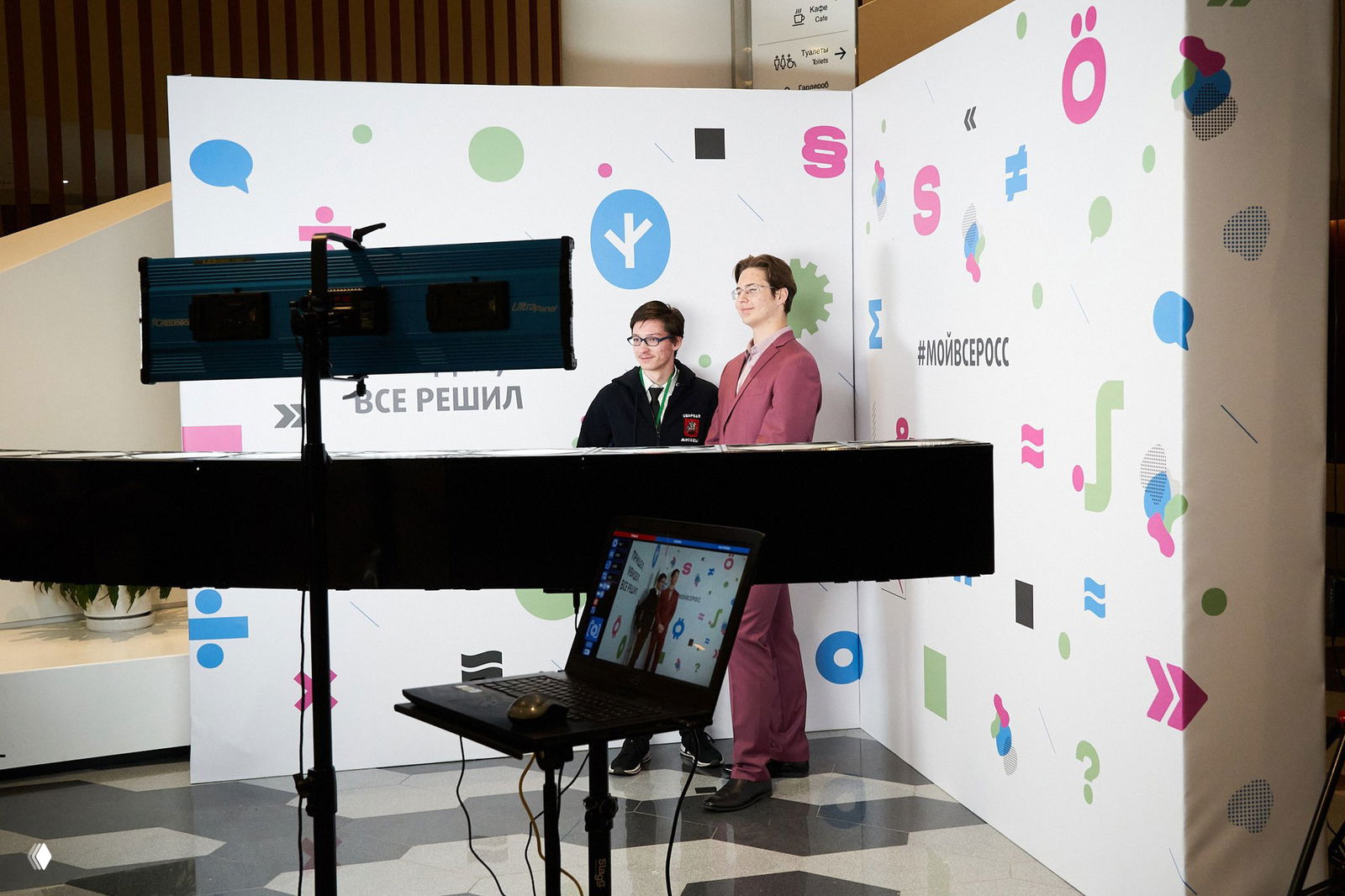 Фотозона Bullet Time: риг с камерами и ноутбук на штативе на переднем плане; двое участников позируют внутри студийной зоны с брендированным фоном.