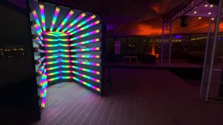 Яркая неоновая фотозона‑туннель с цветными переливающимися трубками в интерьерной локации, подготовленная для фотографий гостей на событии.