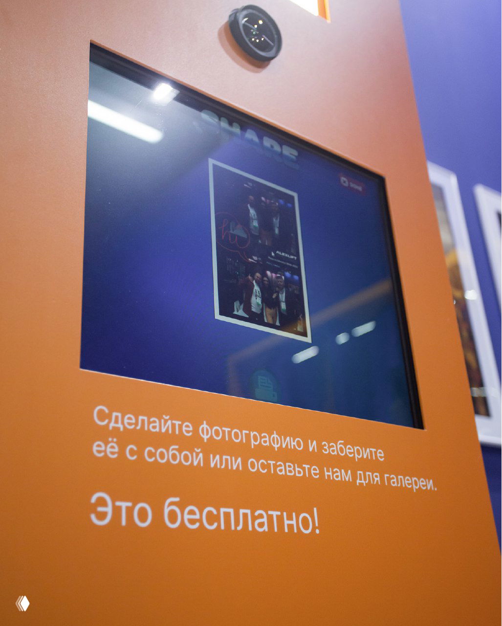 Крупный план экрана фотостойки на оранжевой панели с примером отпечатка и инструкцией, демонстрация интерфейса и области печати для гостей