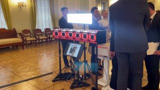 Группа людей у компактной 3D‑фотостойки на корпоративном мероприятии в зале; видна стойка с подсветкой и экраном, люди взаимодействуют с прибором