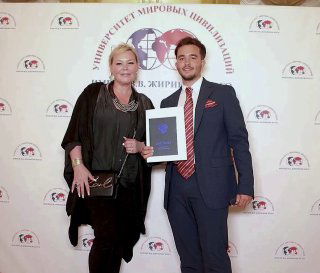 Фотография с вручением сертификата на фоне брендвола, рядом стоит человек в костюме; кадр показывает деловой контекст мероприятий и промо‑атрибутику