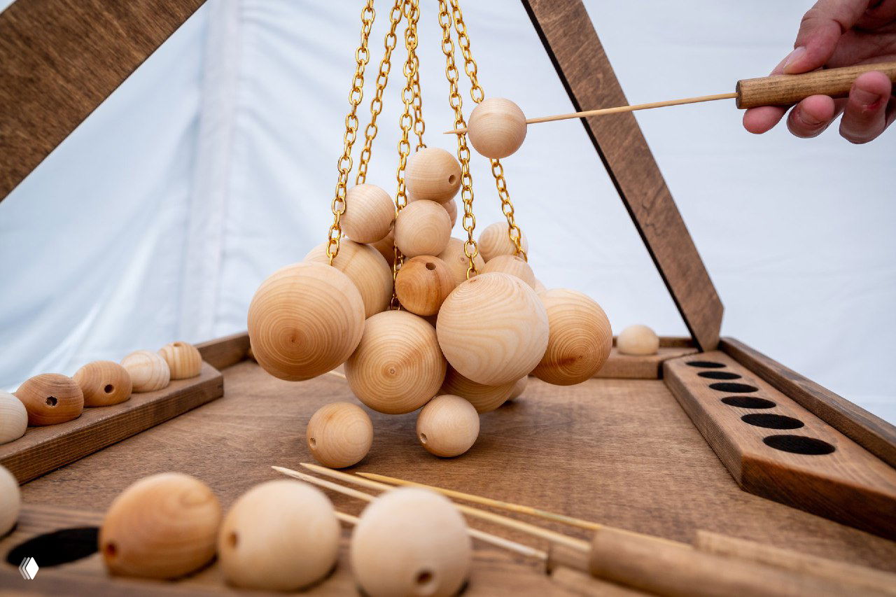 Крупный план крафтовой деревянной настольной игры: деревянные шарики на золотистых цепочках над столом, текстура дерева и детали механики видны отчетливо.