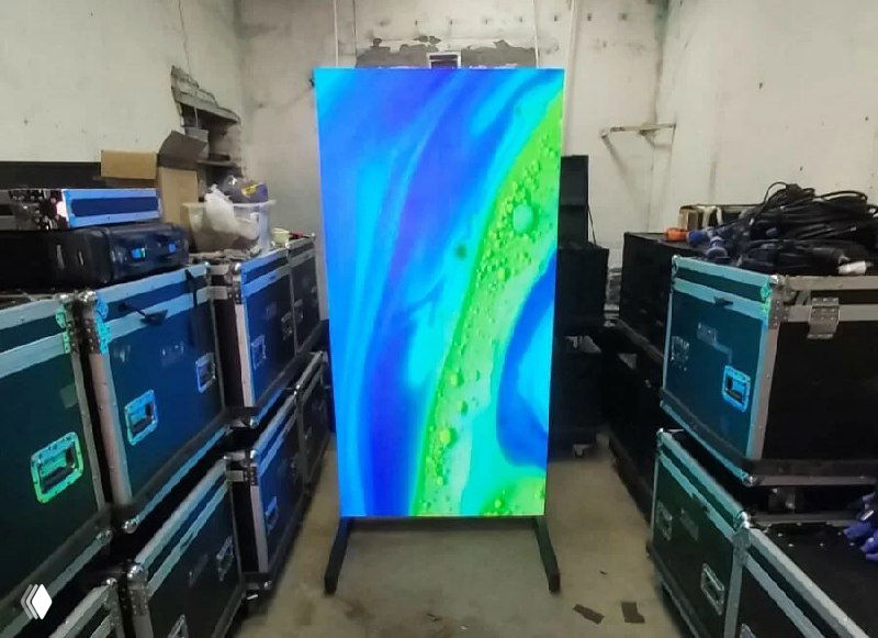 LED‑пилон с ярким абстрактным изображением на экране, установлен в складском помещении между кейсами для оборудования.