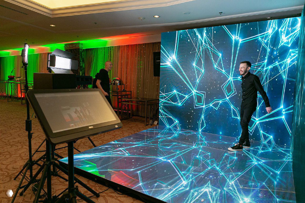 Премиум‑фотозона: светодиодный пол и LED‑экран с неоновой графикой, мужчина позирует; на переднем плане медиа‑киоск и световое оборудование.