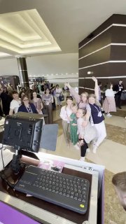 Гости позируют перед селфи‑зеркалом в банкетном зале; в кадре видна рабочая панель фотобудки, экран и клавиатура, создающие интерактивную фотозону.