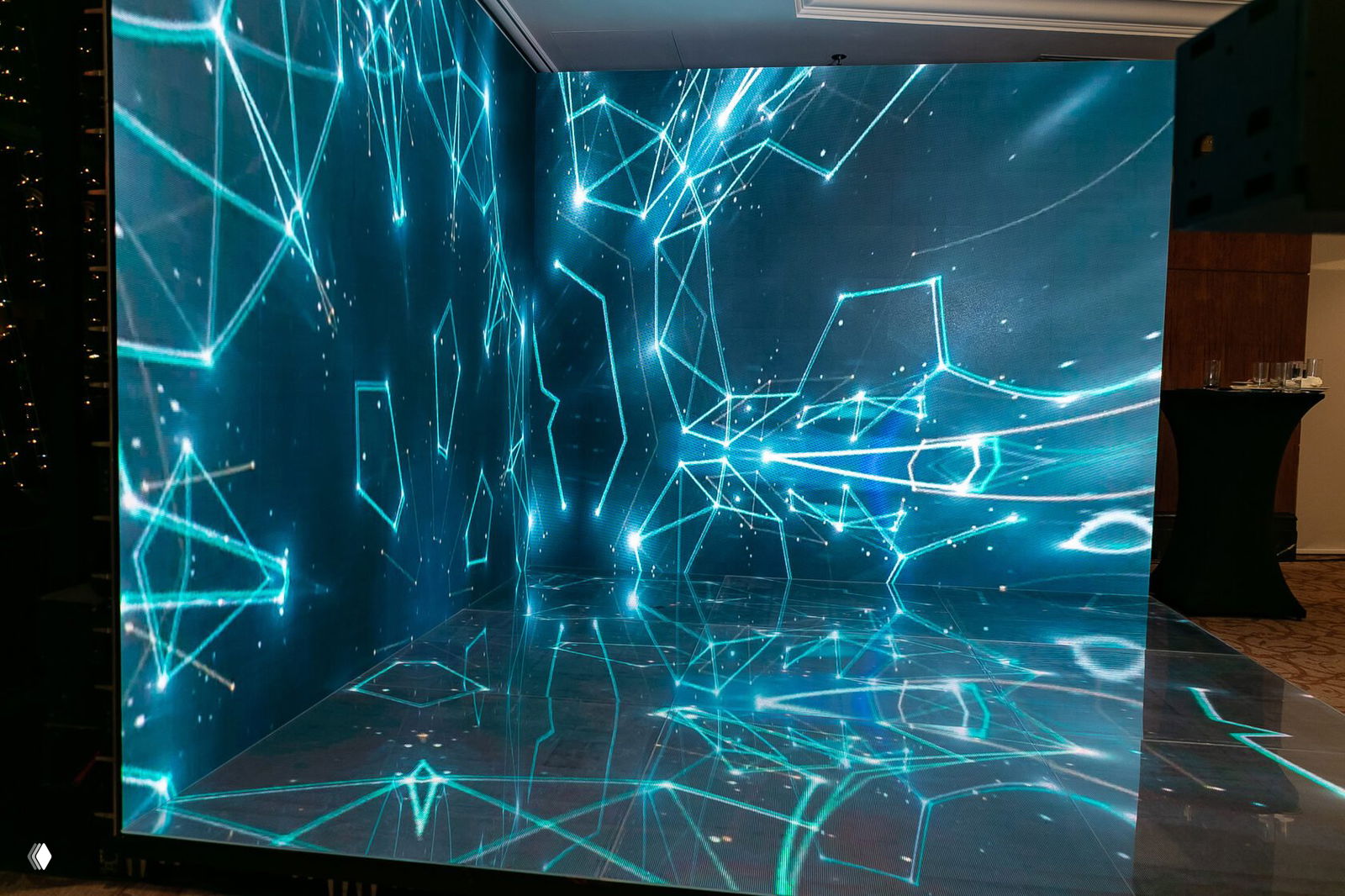 LED‑фотозона из светодиодных экранов в углу банкетного зала с бирюзовыми геометрическими узорами и ярким отражением на полу.