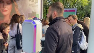 Крупный план фотостойки MixAp сбоку: белый корпус с RGB-подсветкой, участники мероприятия рядом с установкой при дневном свете.