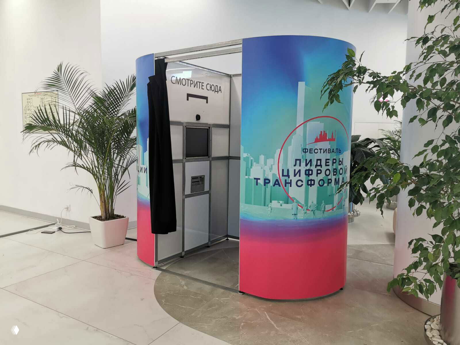 Вид фотокабины внутри: модульная конструкция с монитором и шторкой, на наружных панелях видна графика фестиваля и логотипы спонсоров.
