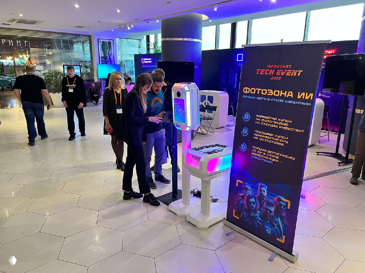 Широкий кадр выставочной зоны: несколько посетителей вокруг белой подсвеченной фотостойки с ИИ и стоящий рядом ролл‑ап с рекламой мероприятия.