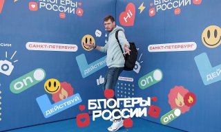 Мужчина позирует на синем фоне с логотипом «Блогеры России», стикерами и элементами фотозоны — пример оформления для событий.